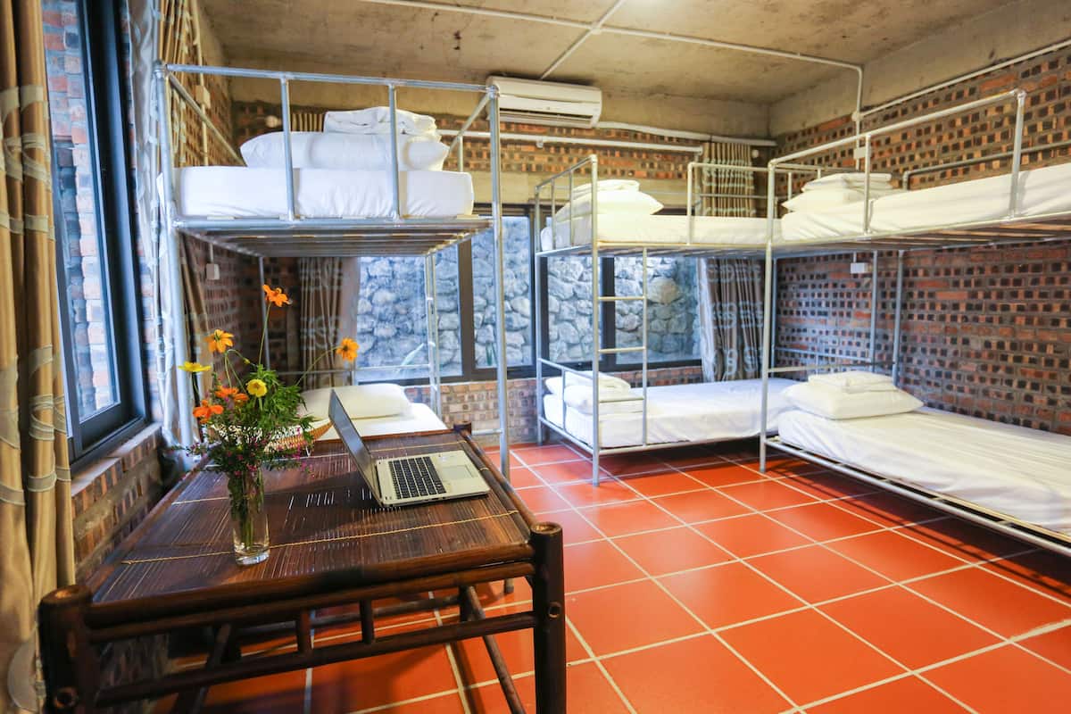 Une chambre de dortoir avec des lits superposés, un ordinateur portable posé sur une table en bois et un vase rempli de fleurs.