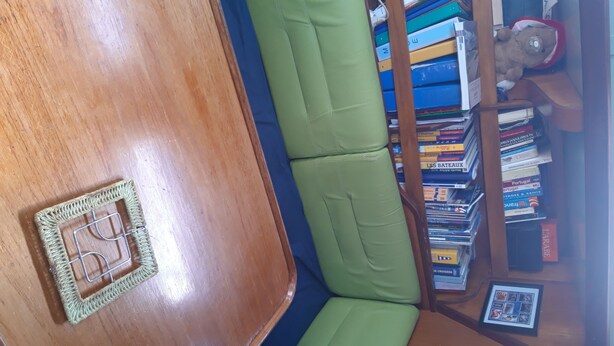 Un angolo di stanza con un tavolo di legno, una panca imbottita verde e una libreria piena di libri.