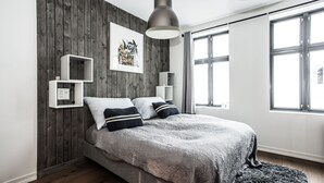 Une chambre moderne avec un mur en bois, un grand lit avec une literie à motifs, un luminaire suspendu et une fenêtre avec des rideaux.