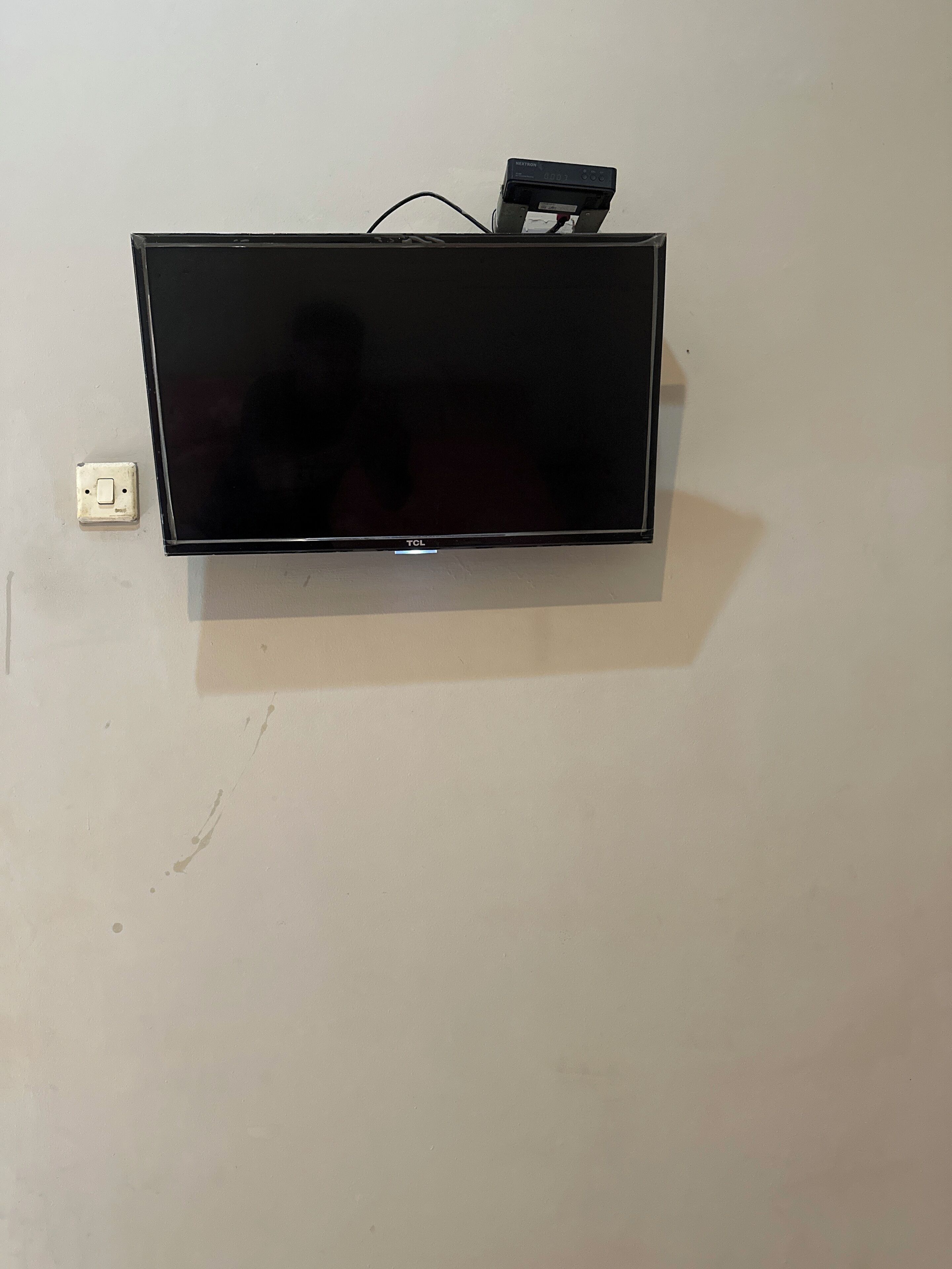 A flat-screen TV mounted on a wall with a power outlet to its left.