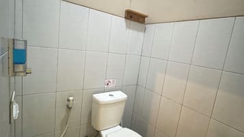 Un bany petit amb un vàter, un cubet blau i parets revestides de rajoles.