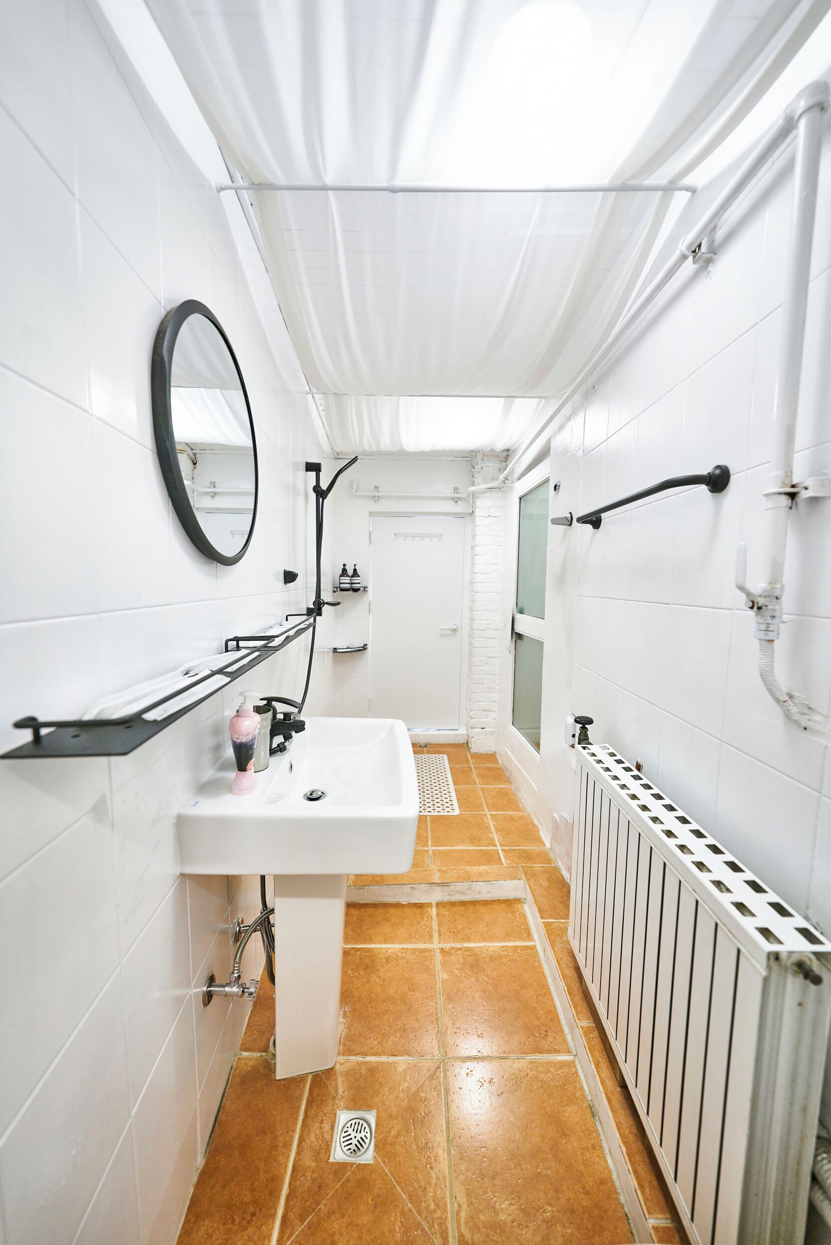 Ein Badezimmer mit weiß gefliesten Wänden, einem weißen Waschbecken, einem Spiegel und einer Duschkabine.