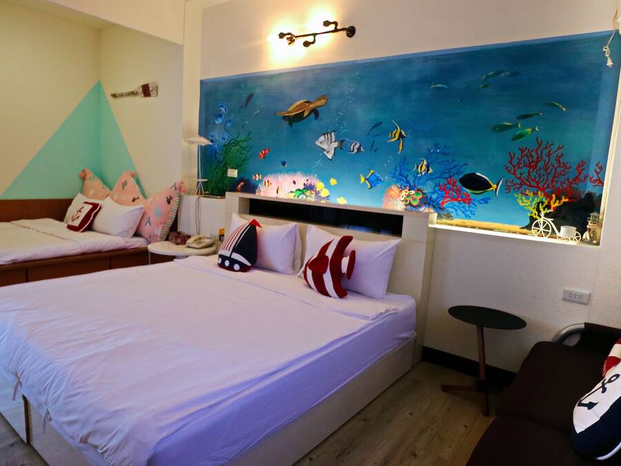 A hotel room with two beds, a large wall mural of an underwater scene, and a small table with a chair.