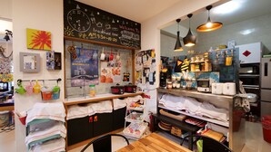 Cafetería para desayunos con pizarra de menú, zona de cocina y diversos alimentos a la vista.