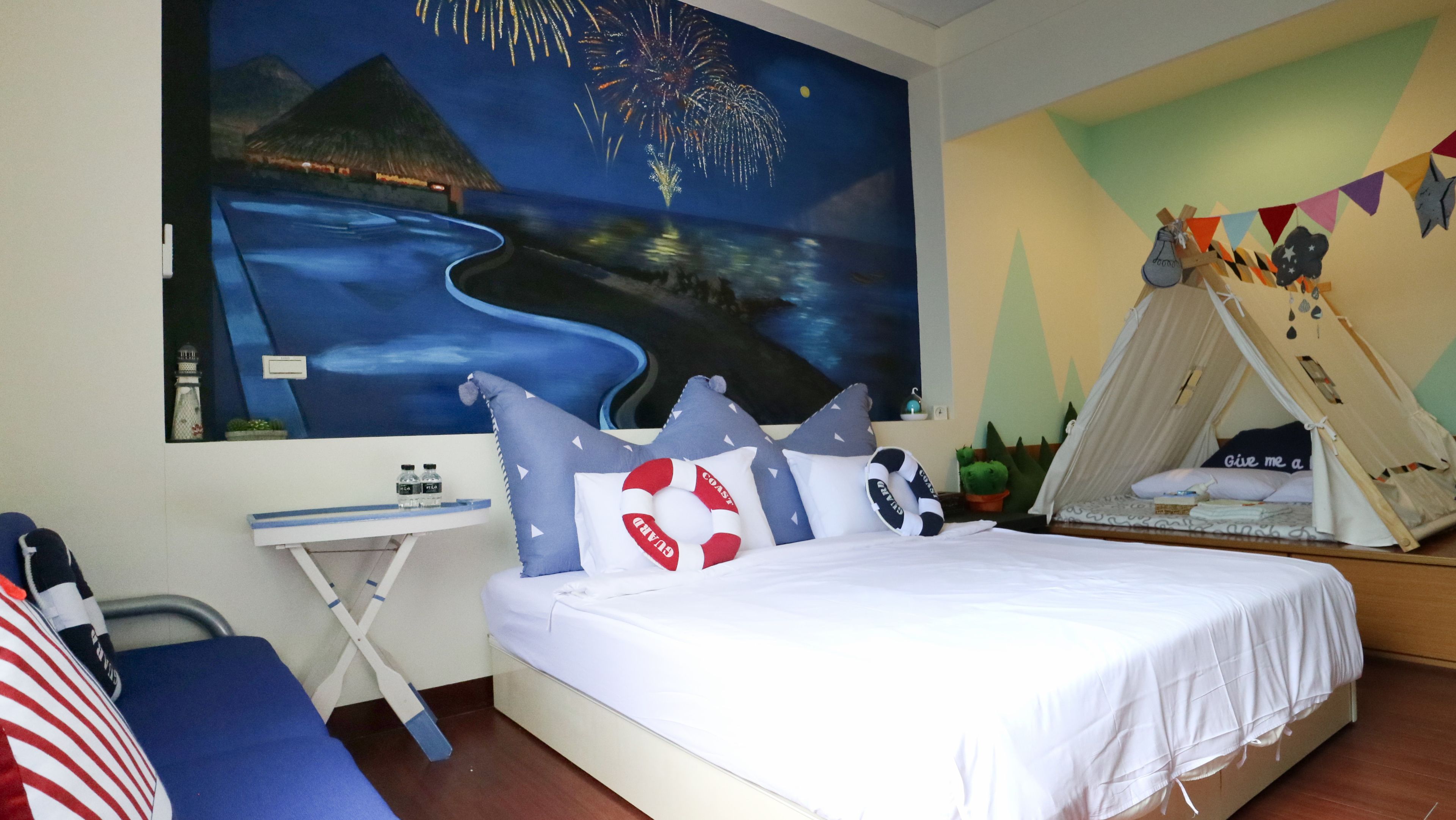 Ein Schlafzimmer mit Bett, Schreibtisch, Stuhl, einem Zelt und einem Wandbild mit Feuerwerk.