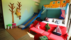 Un cuarto de juegos infantil con un tobogán, una decoración de jirafa y un mural de pared colorido.