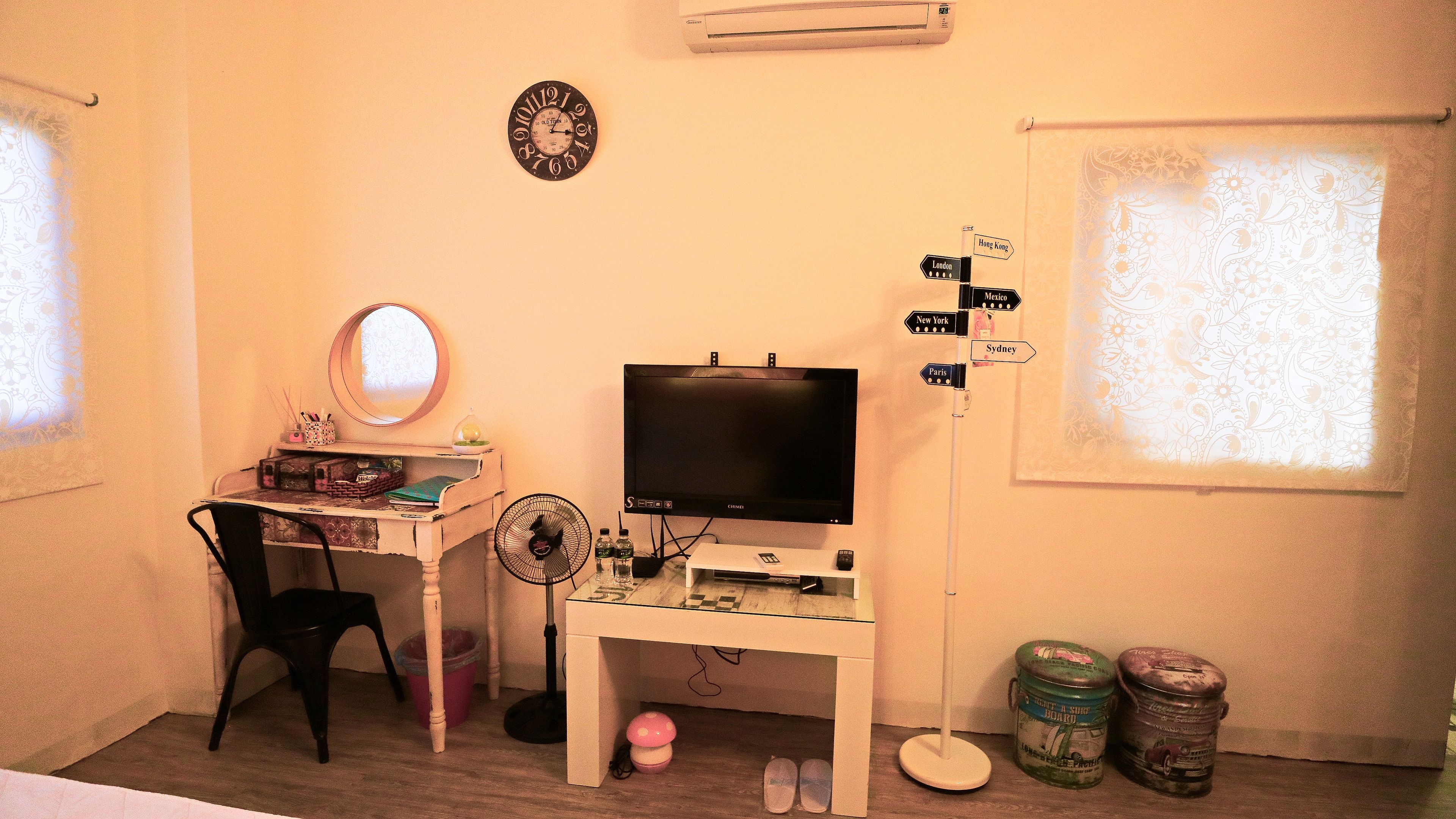 A room with a television, a desk with a chair, a mirror, and a wall clock.