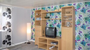 Un salon avec un meuble de rangement en bois pour l’équipement audiovisuel, un téléviseur et un papier peint à motifs floraux.