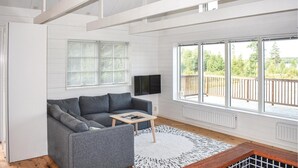 Ett modernt vardagsrum med en grå soffa, ett litet träbord och ett stort fönster med utsikt över grönområden.