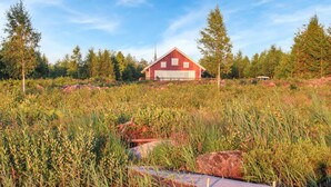 En röd ladugård med en vit garageport, omgiven av tät vegetation och träd.