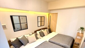 A bedroom with two beds, a mirror, a ceiling light, and a small wooden side table. - Reve K 302 (Naha)