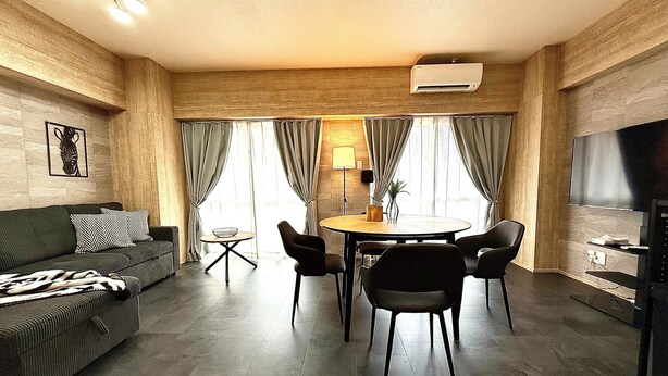 A modern living room with a sofa, a dining table with chairs, a TV, and a wall-mounted air conditioner. - Reve K 302 (Naha)