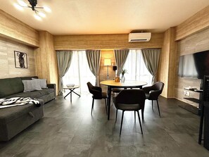 Un salon moderne comprenant un canapé, une table à manger avec des chaises, un téléviseur et un climatiseur fixé au mur.
