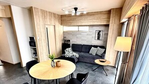A modern living room with a sofa, a round table with chairs, and a dining area. - Reve K 302 (Naha)