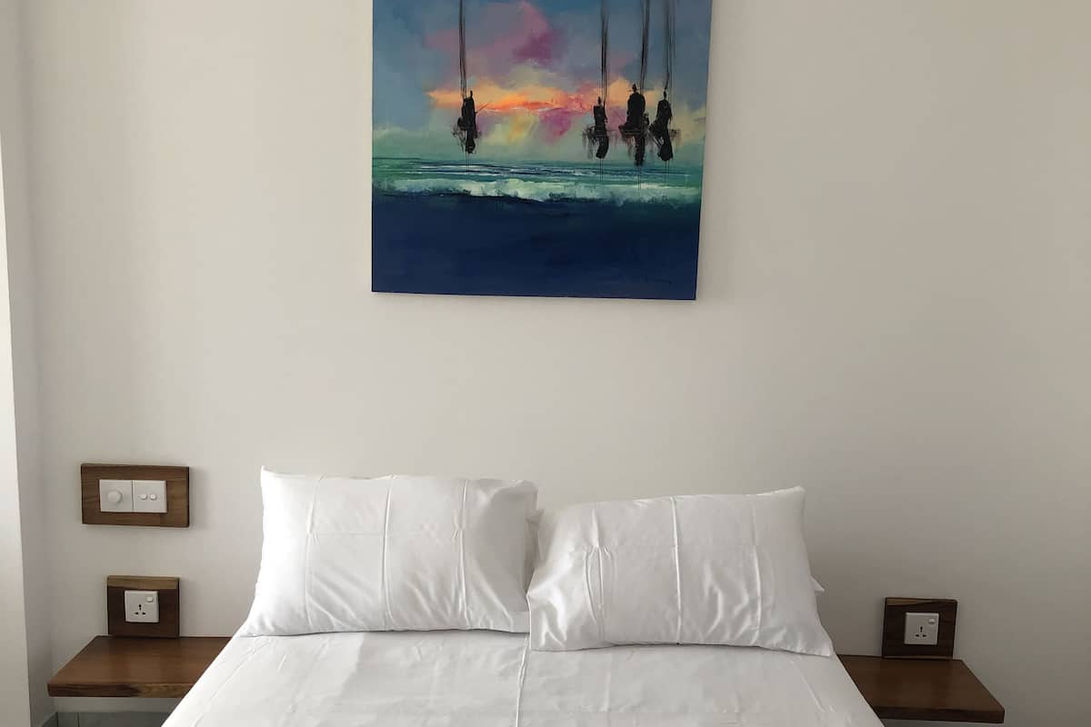 A bedroom with a large bed, white bedding, two bedside tables with lamps, and a painting of sailboats on the wall.