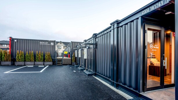 A modern hotel entrance with a metal facade, a parking area, and a visible guest room with a bed and a small table. - HOTEL R9 The Yard KANUMA NISHIMORO (Kanuma)
