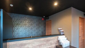 A reception area with a counter, a tiled wall, and a wooden door. - HOTEL R9 The Yard KANUMA NISHIMORO (Kanuma)
