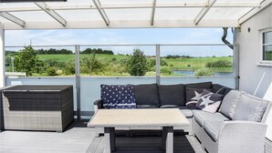 Un espacio de estar techado al aire libre con sofá y mesa, con vistas a un paisaje verde.
