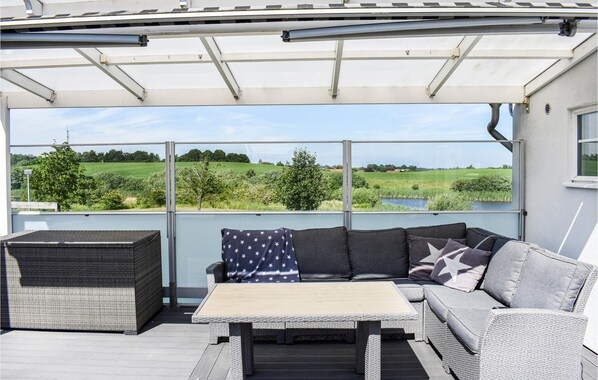 A covered outdoor seating area with a sofa and table, overlooking a green landscape.