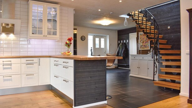 Una cocina moderna con armarios blancos, una isla de madera y una escalera negra.