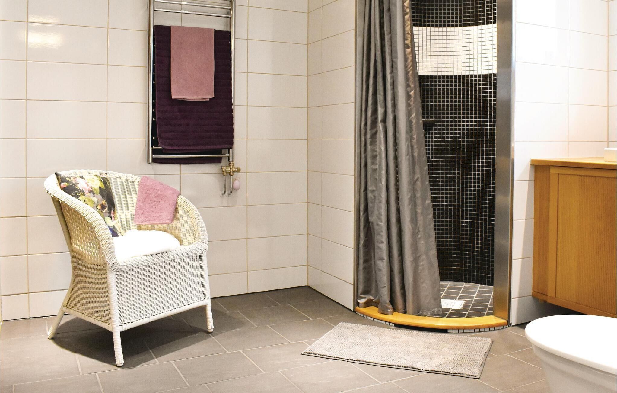 A bathroom with a shower, a white wicker chair, a toilet, and a sink.