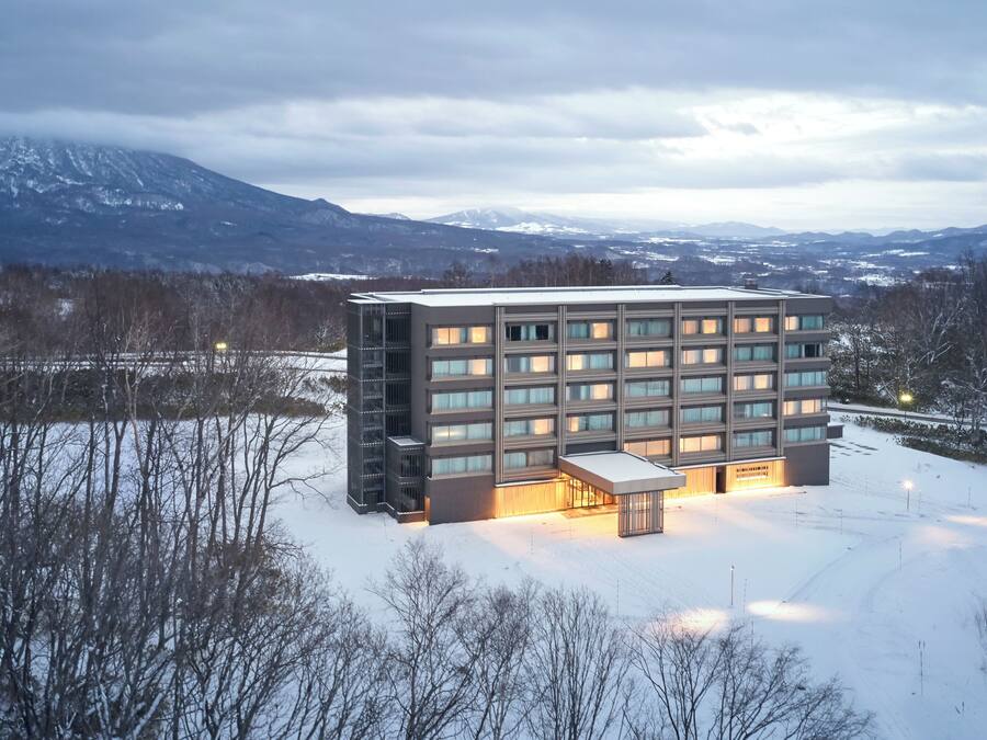 A modern building with multiple floors and large windows, surrounded by a snowy landscape and mountains in the background.