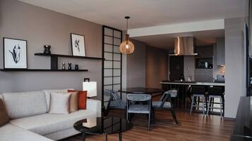 A modern living room with a sofa, coffee table, and chairs, a kitchen area with a dining table, and a hanging light fixture.