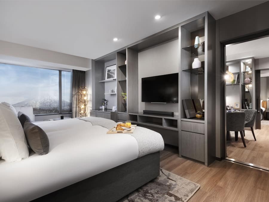 A modern bedroom with a large bed, built-in TV, and a dining area.