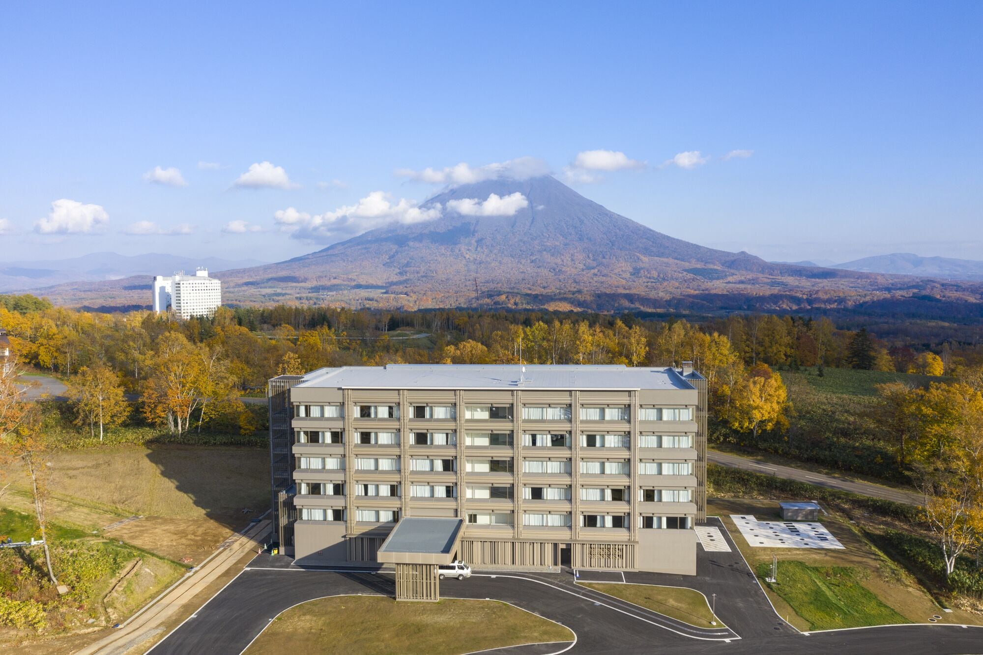 A modern multi-story hotel with a central courtyard, surrounded by autumn foliage and a mountain in the background.
