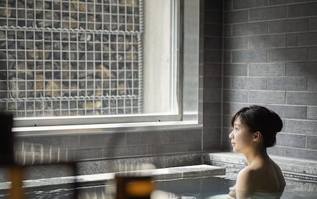 A person in a hot spring with a window and tiled walls.