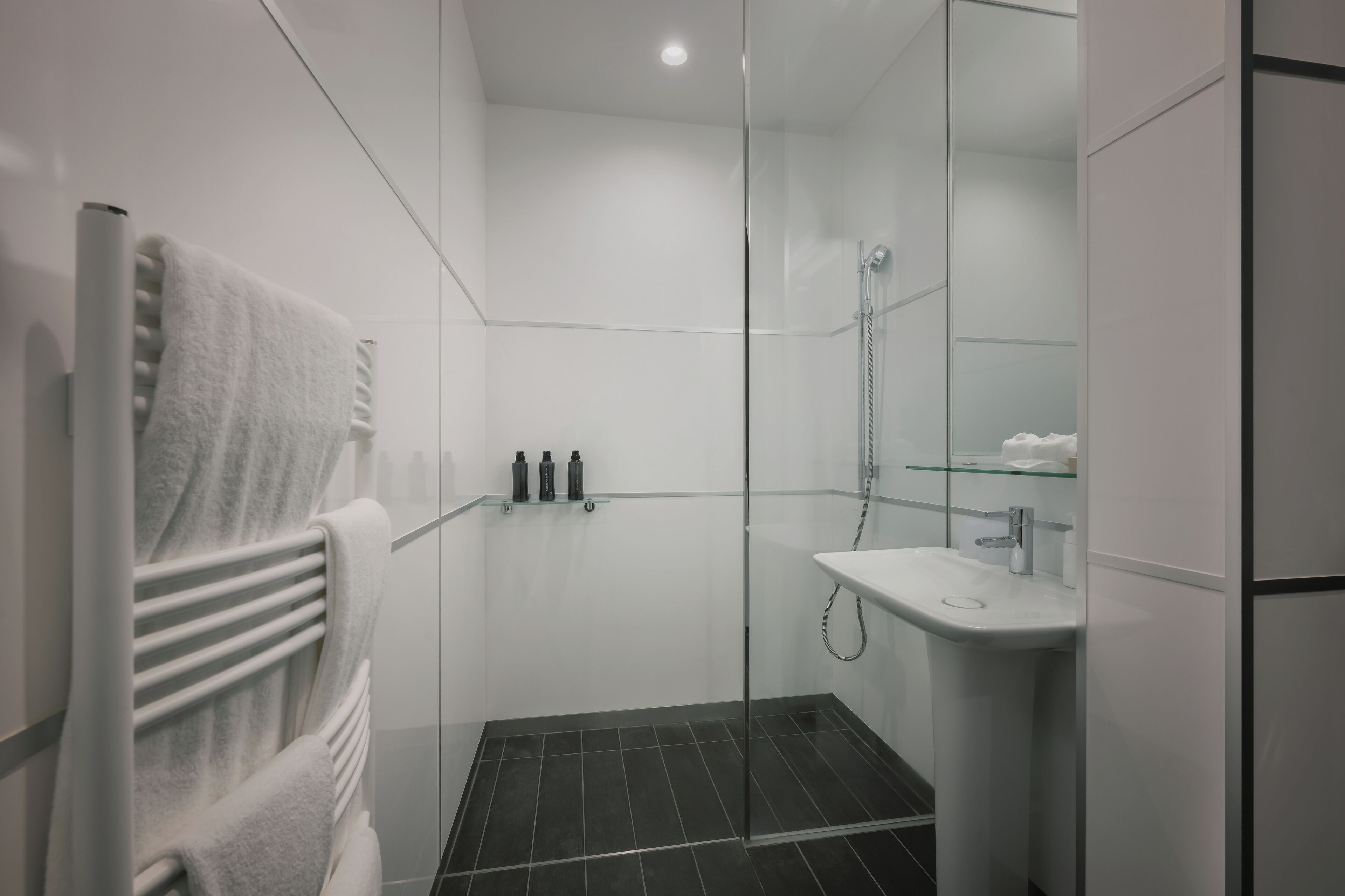 Un baño moderno con cabina de ducha de vidrio, un lavabo blanco y un perchero para toallas.