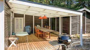 Un patio techado con una mesa y sillas de madera, una parrilla de barbacoa y una mesita con una lámpara.