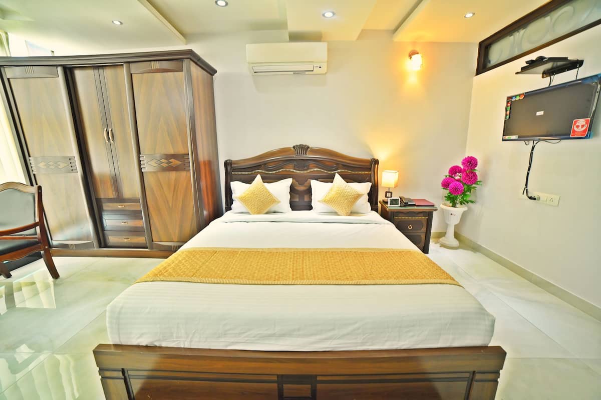 Ein ordentlich eingerichtetes Hotelzimmer mit einem großen Bett, einem Schrank, einem Fernseher und einem Nachttisch mit Lampe und Blumen.