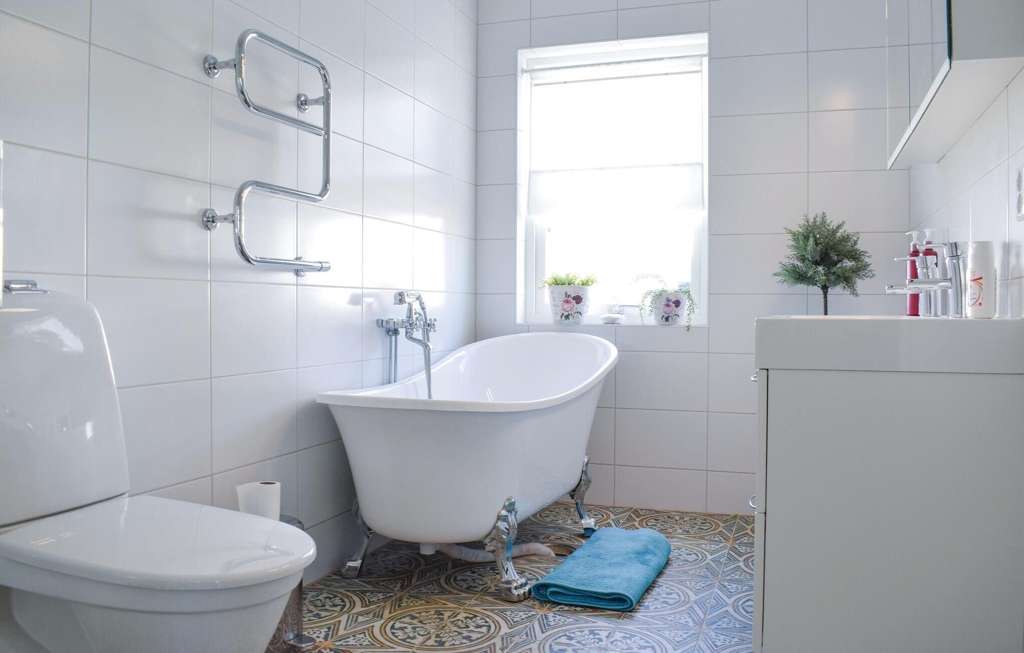 Et badeværelse med et hvidt badekar, toilet og gulvfliser med et mønster.