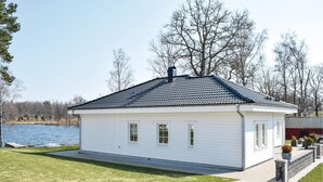 Yhden kerroksen korkuinen valkoinen talo, jossa on tumma katto, pieni kuisti ja näkymä järvelle.
