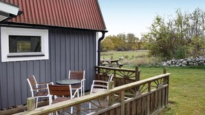A rustic cabin with a metal roof, a deck with wooden chairs and a table, and a stone wall in the background. - 2 bedroom gorgeous home in Jämjö (Jämjö)