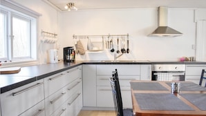 A modern kitchen with white cabinets, a black countertop, a built-in oven, and a dining area with a wooden table and chairs. - 2 bedroom gorgeous home in Jämjö (Jämjö)