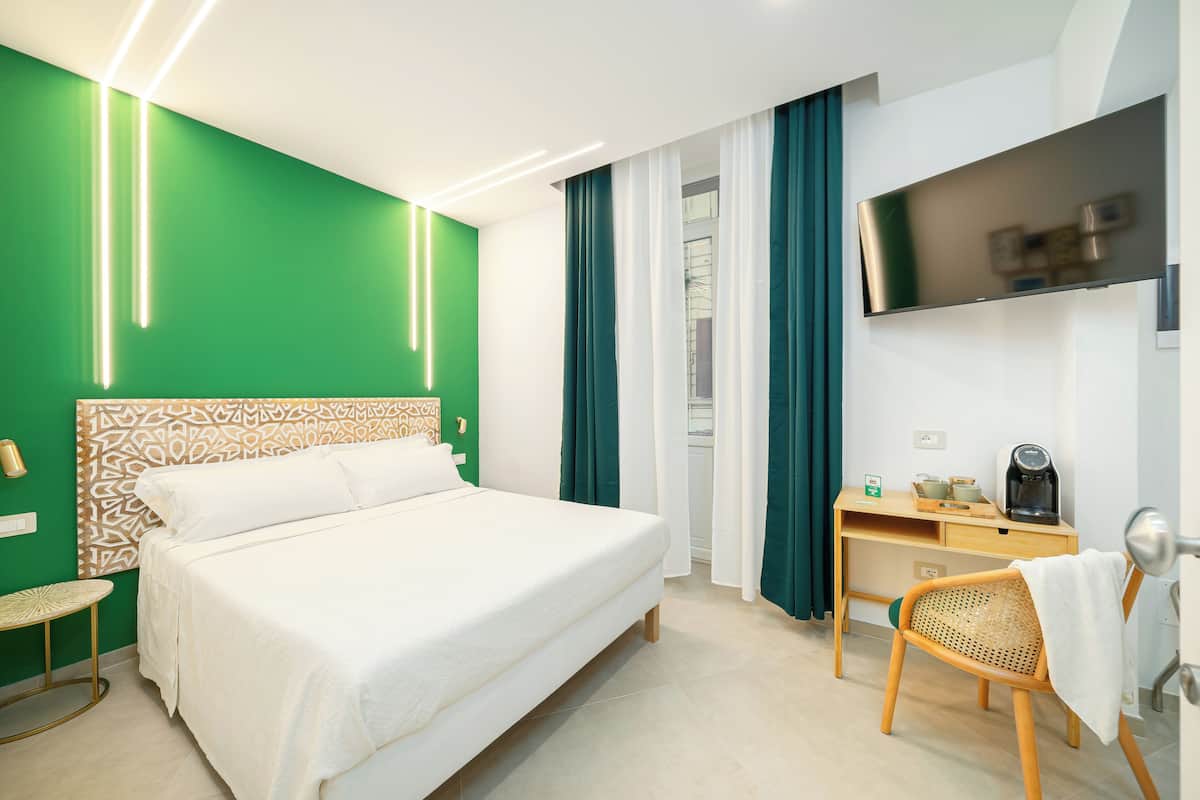 A hotel room with a bed, a desk, a chair, a TV, and a green accent wall.