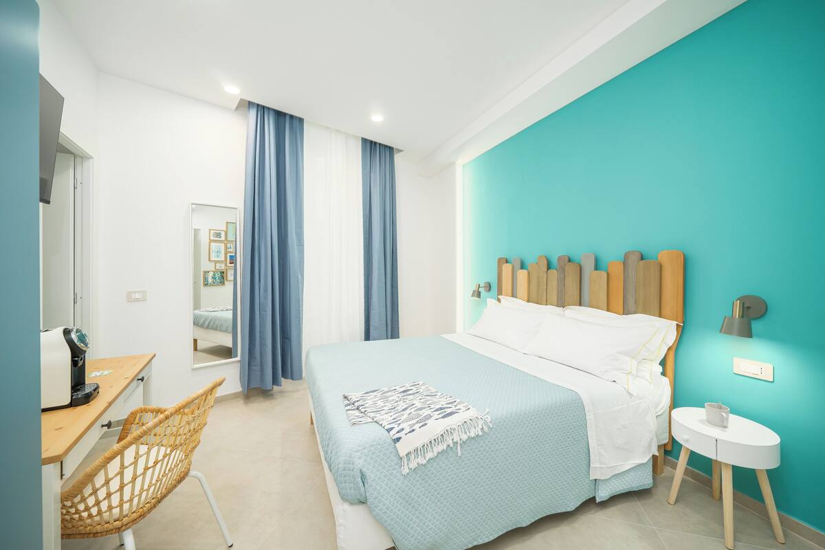 A bedroom with a bed, a desk, a chair, and a small table.
