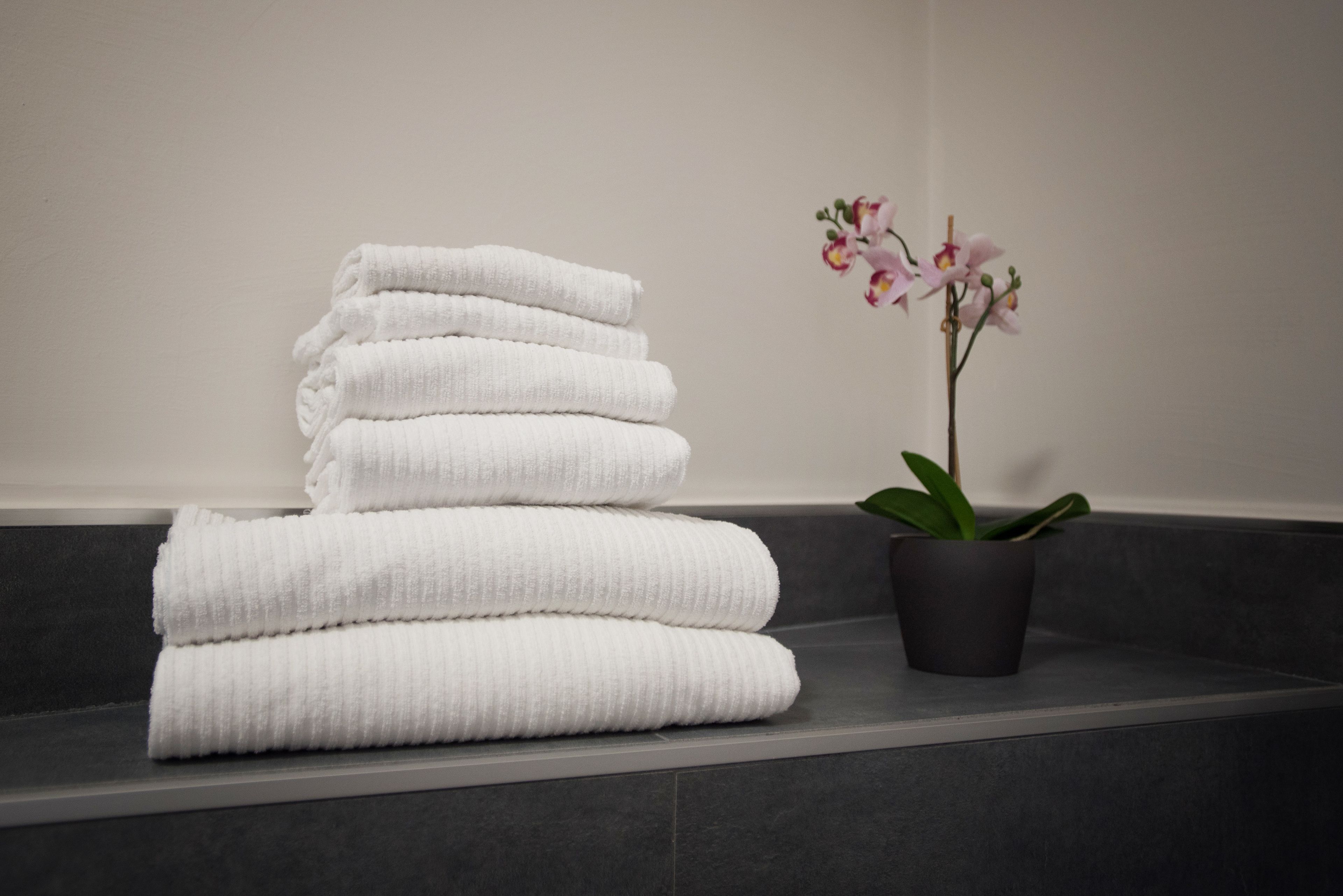 A stack of white towels on a dark gray surface next to a potted orchid plant.