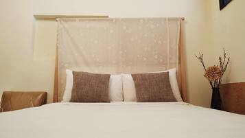 A neatly made bed with a canopy, two pillows, and a vase with dried flowers on a nightstand.