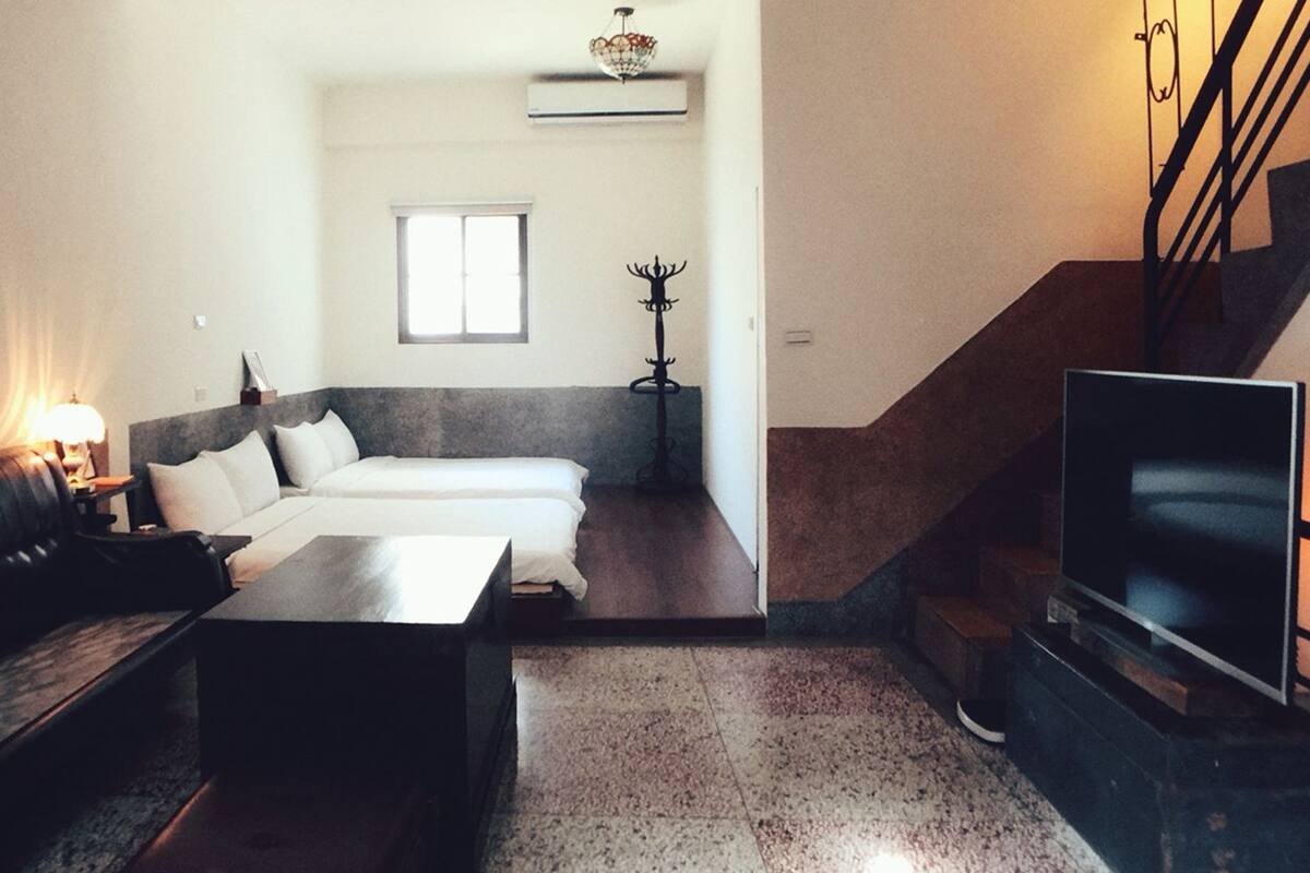 A modern living room with a sofa, a coffee table, a TV, a staircase, and a window.