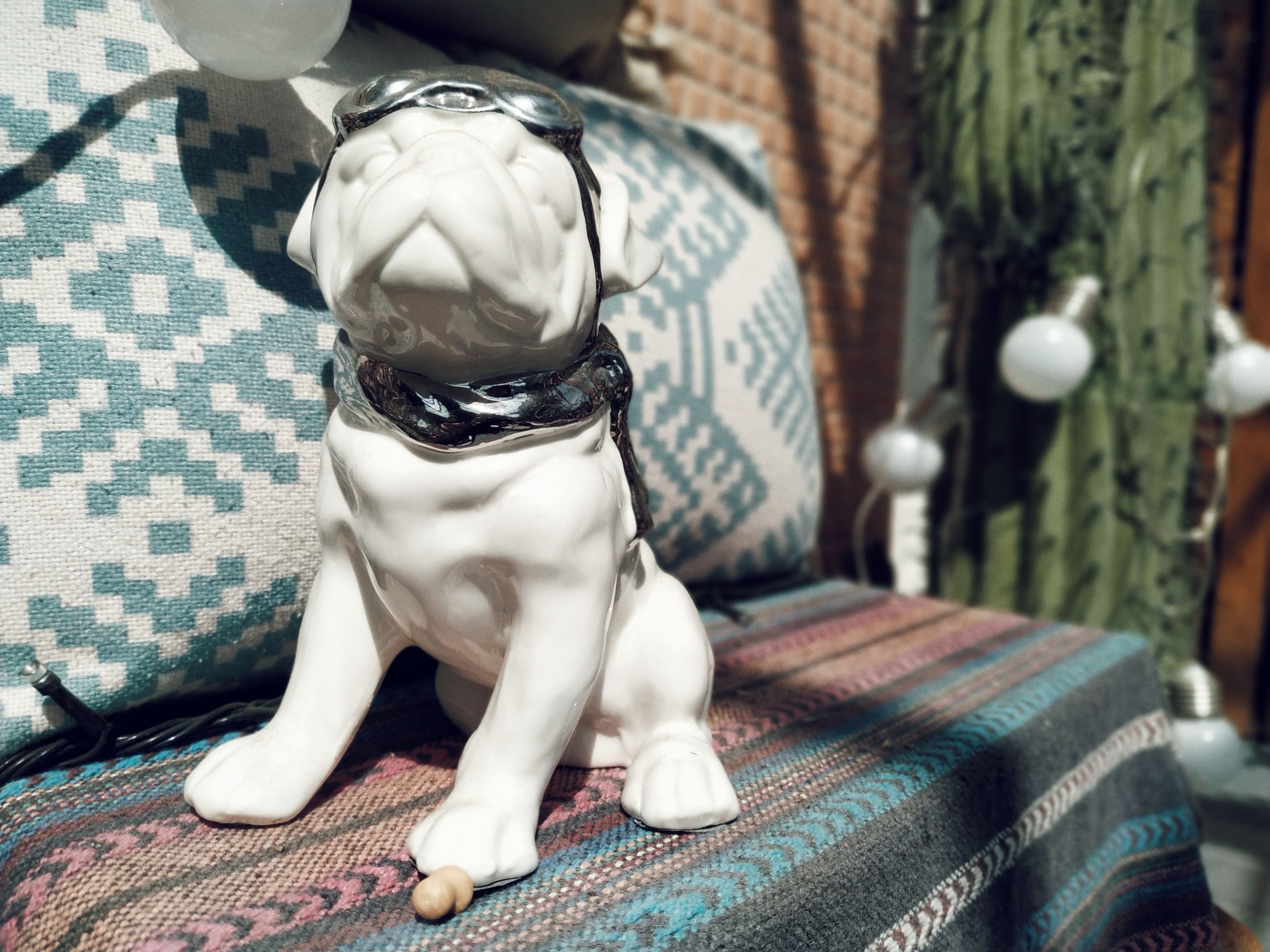 Une figurine de chien en céramique blanche, portant des lunettes, est assise sur un canapé à motifs.