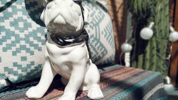 Une figurine de chien en céramique blanche, portant des lunettes, est assise sur un canapé à motifs.