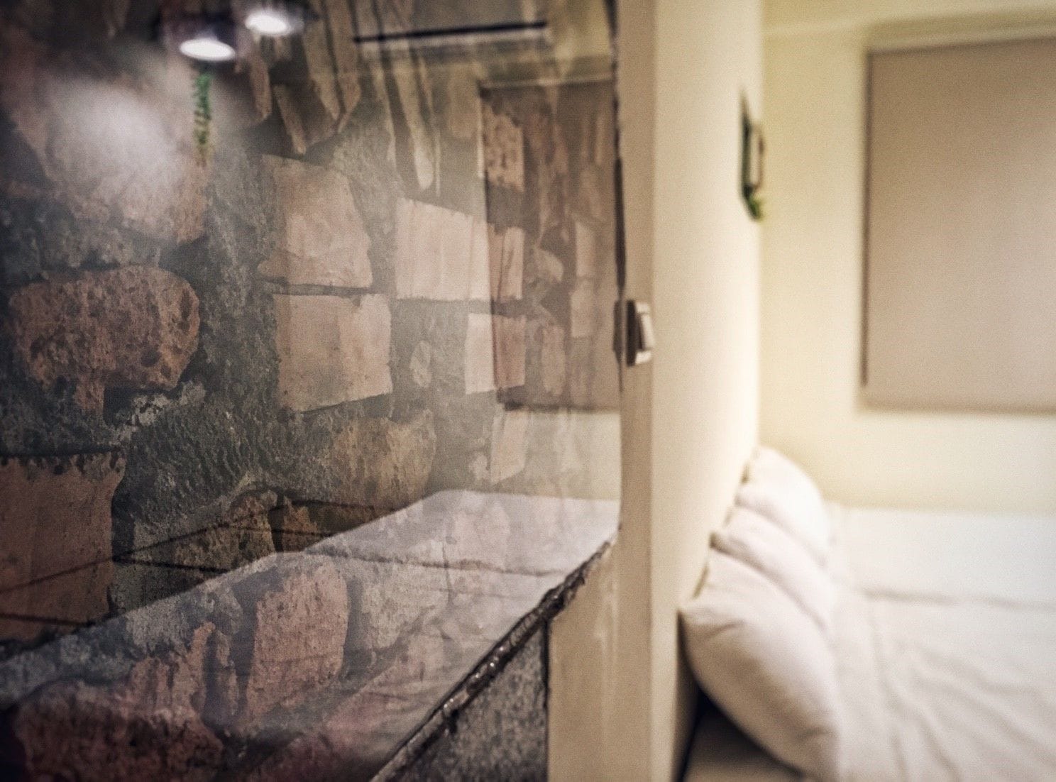 A stone wall with a wooden ledge, a door, and a bed with white bedding.