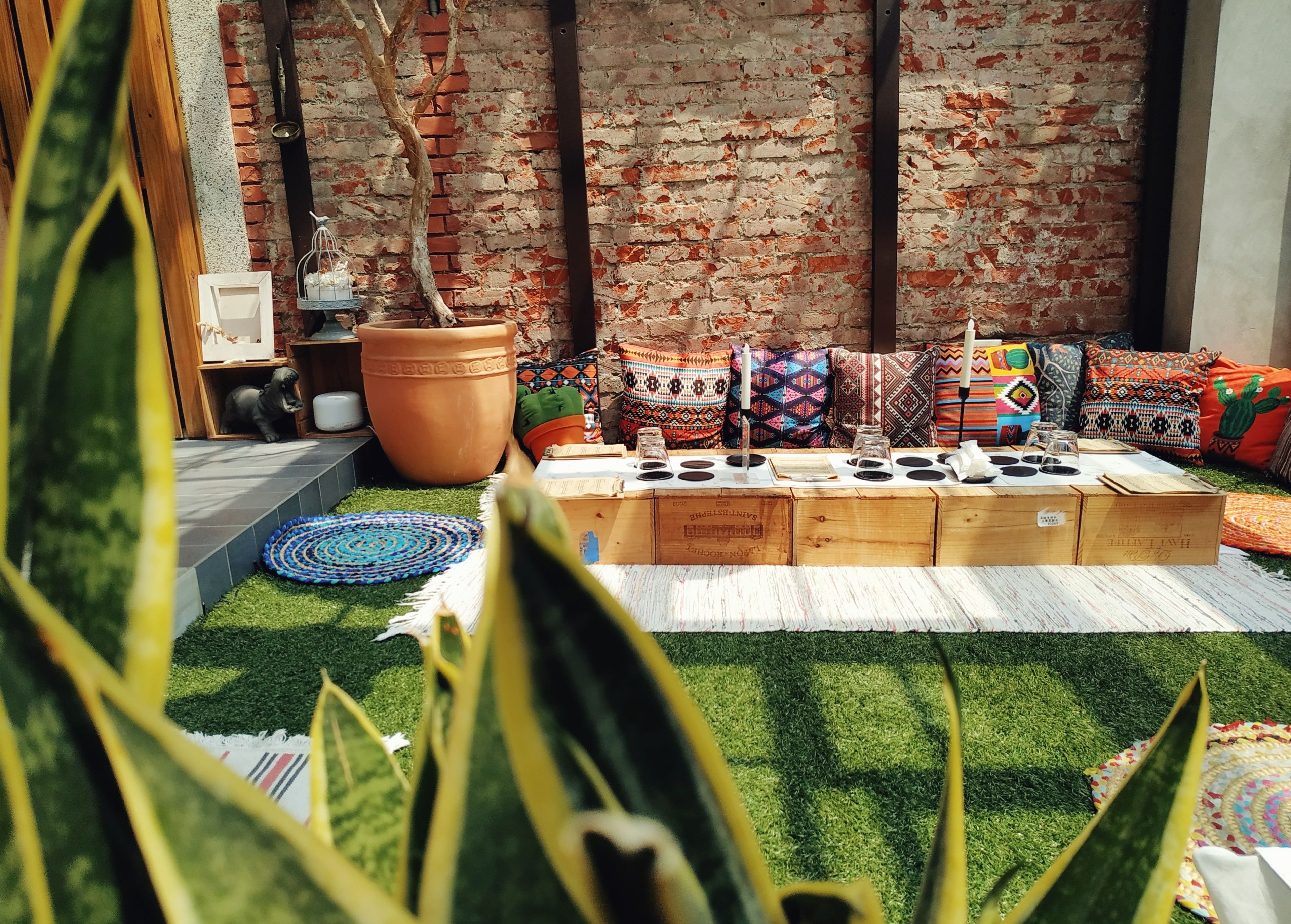 A cozy outdoor seating area with a brick wall backdrop, a large terracotta pot, and colorful cushions.