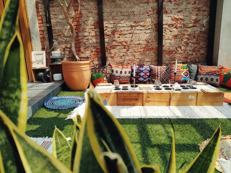 A cozy outdoor seating area with a brick wall backdrop, a large terracotta pot, and colorful cushions.