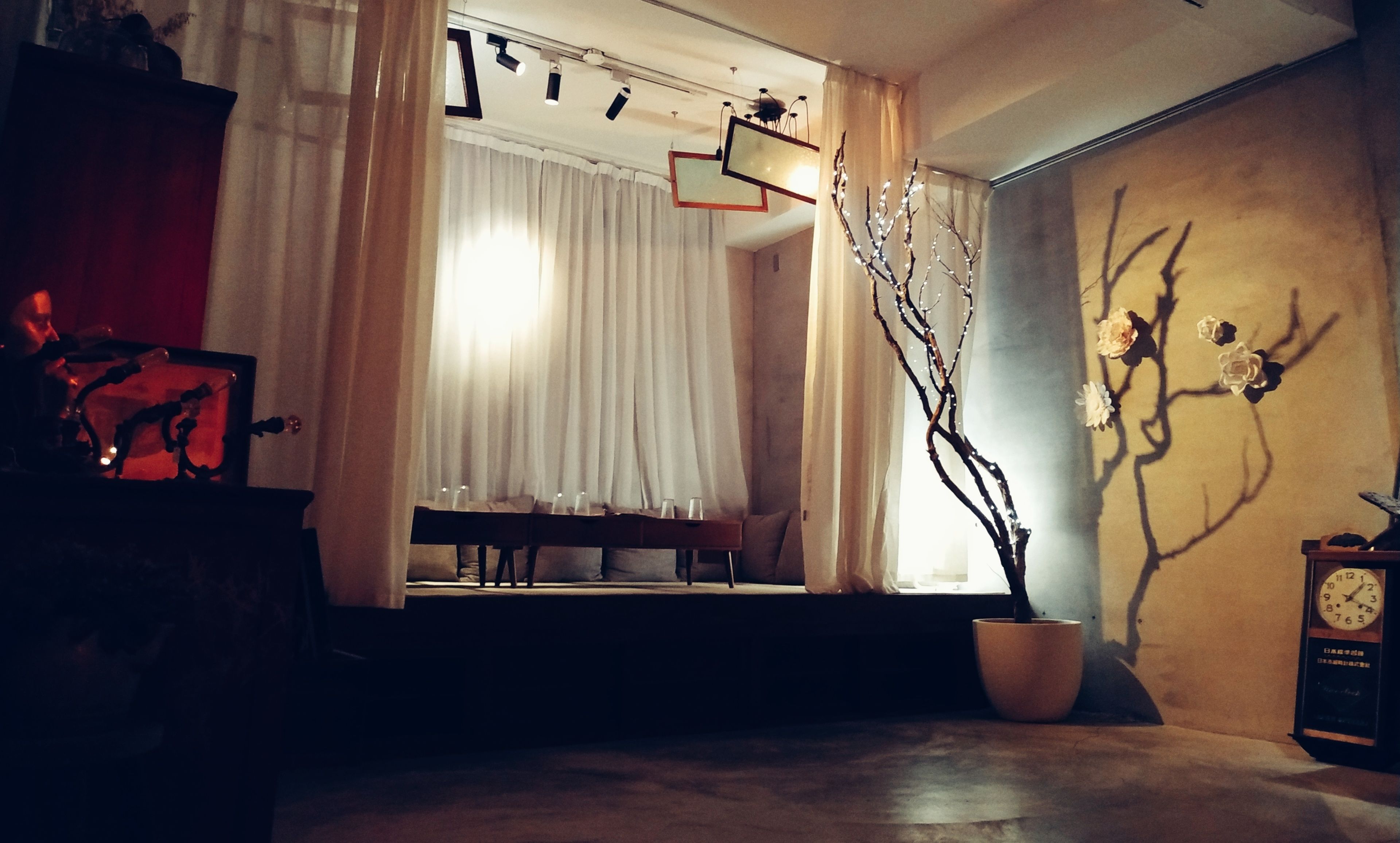 A dimly lit room with a sofa, a table with glasses, a potted plant, and a wall clock.