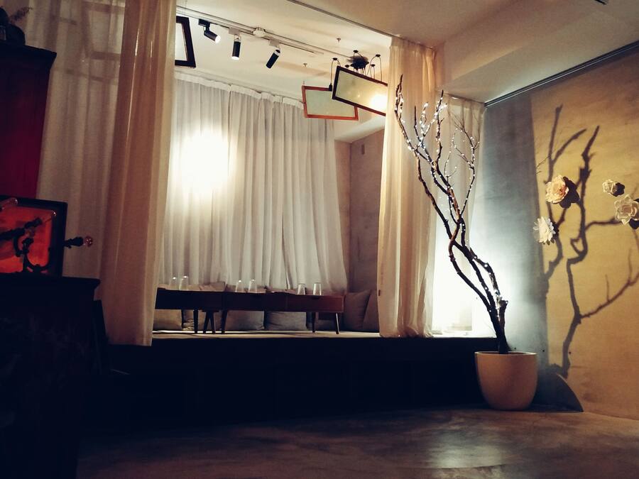 A dimly lit room with a sofa, a table with glasses, a potted plant, and a wall clock.