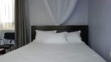 A neatly made bed with white linens in a room with light blue walls and a dark headboard.